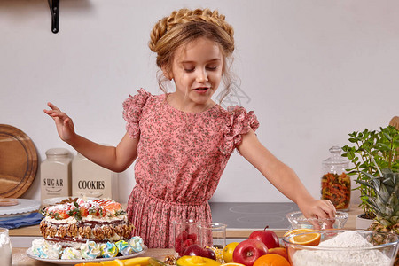 穿着粉红色连衣裙的漂亮孩子正在厨房做一个自制蛋糕图片