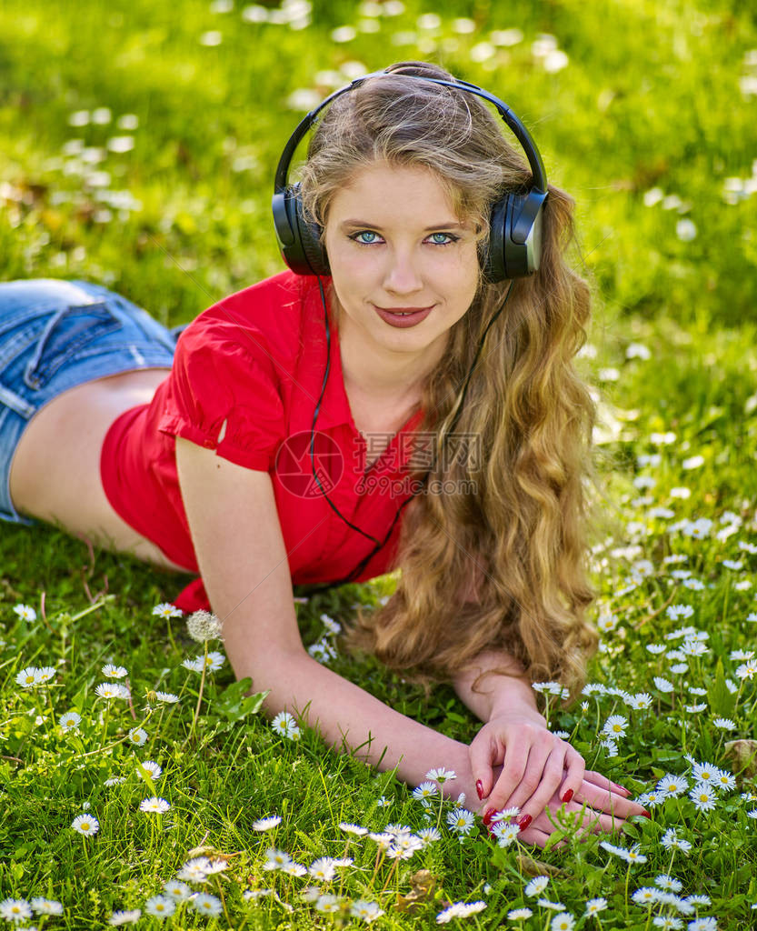 戴耳机的女孩在绿草上用洋甘菊花夏季户外捕捉节奏音乐步行可以提高记图片