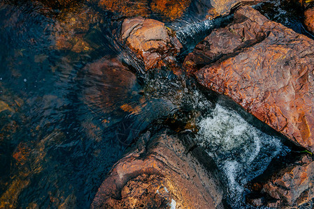 泉水特写中的光滑石头干净的水流在红色和橙色的石头之间山泉溪流的多彩自然背景与复制空间美丽的小溪背景图片