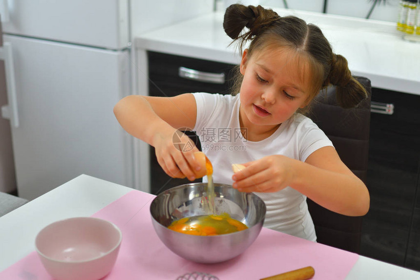 女孩打破了鸡蛋小女孩在家里的厨房里准备饼干这时蛋黄落入金属碗中烹饪自制食物专注图片
