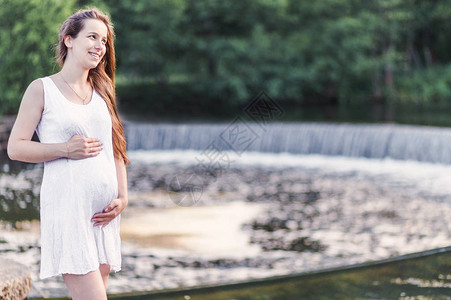 一位美丽的孕妇的相片她站在河岸附近图片