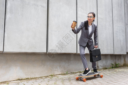 身着正式服装的快乐女商人在滑板上骑车图片