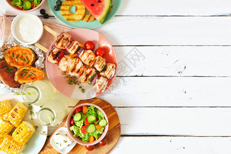 夏季BBQ或野餐边界选择烤肉水果沙拉和土豆在白色木质背景的视图之上图片