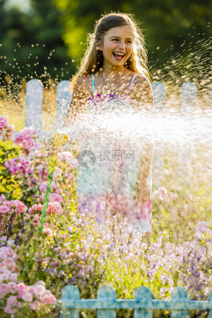 俏皮的女孩在夏天的一天在花园里用雨浇花孩子在阳光明媚的日子在日落时使用花园软管小园丁图片