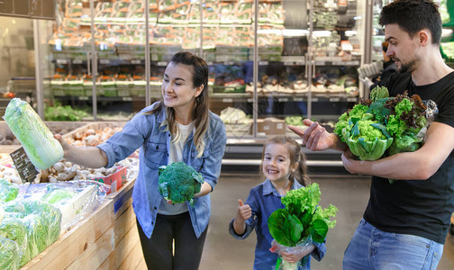 幸福的夫妻带着孩子买菜快乐的三口之家在超市或场的蔬菜部选图片