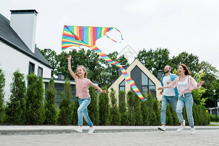 幸福的孩子在街头快乐的父母身边带着多彩风筝跑图片
