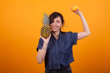 在黄色背景的工作室里用热带水果笑年轻漂亮的女人美味的凤梨美味的菠图片