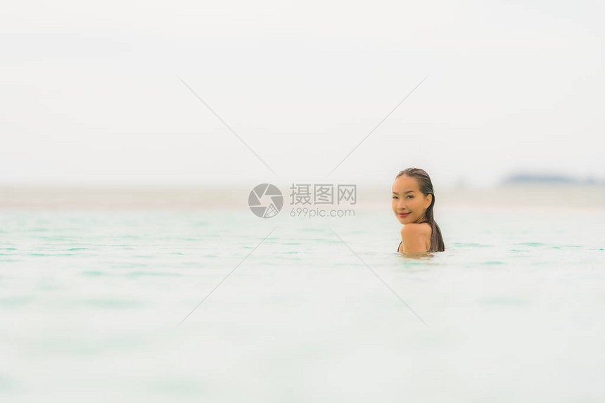 肖像美丽的亚洲年轻女穿着比基尼在酒店度假村的游泳池周围图片