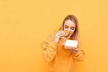 有趣的女孩站在黄色背景上的一包和汉堡图片