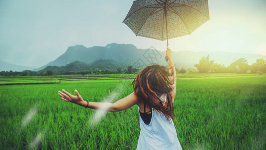 亚洲女旅行在假期放松妇女们站在雨伞里在雨季期间的草地上旅游绿色稻田雨图片
