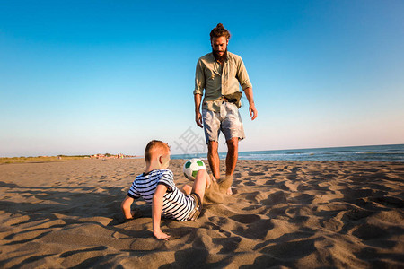 快乐的父亲和儿子在沙滩上踢足球在暑假享受愉快的家庭时光图片