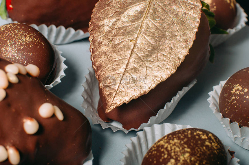 用可食用的金巧克力叶装饰的牛奶巧克力覆盖的美味草莓的特写镜头图片