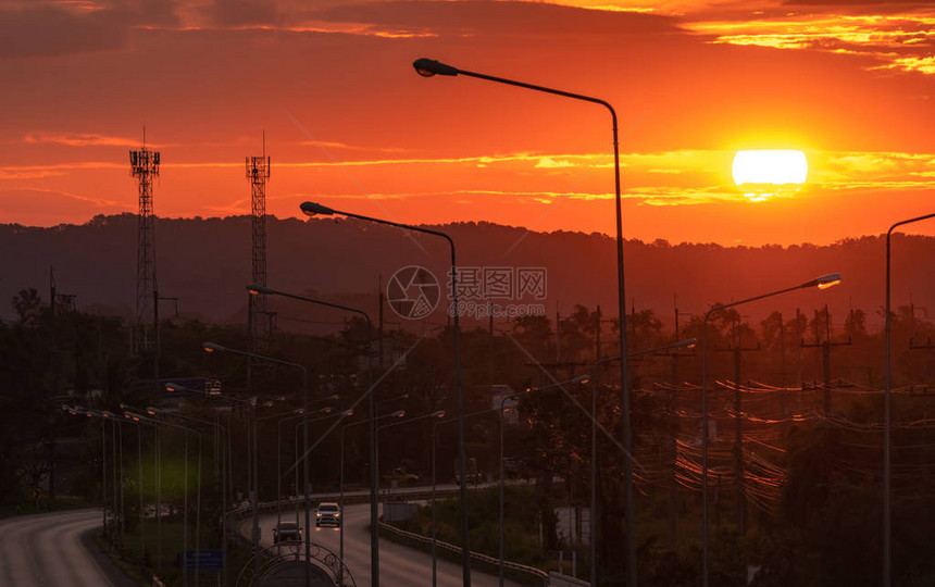 早上在山上的美丽日出大太阳在橙色和红色云彩之间的早晨升起早上在曲线柏油路上开车的人去的天空图片