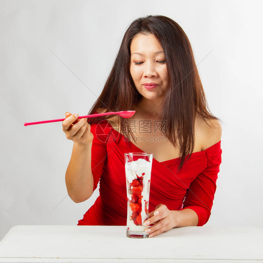 穿红裙子的亚洲美女吃着美味的草莓水果甜点白桌在白色背图片