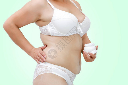 一个穿着白色内衣的超重女在腹部和大腿上涂抹乳霜图片