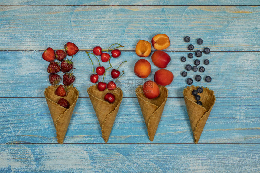 浆果和水果冰淇淋在蓝色木质背景的华夫饼锥中平铺各种新鲜水果蓝莓草莓樱桃杏夏季甜美菜单概念自图片