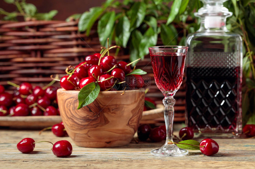 樱桃酒和红樱桃放在花园的木桌上的木碗里图片