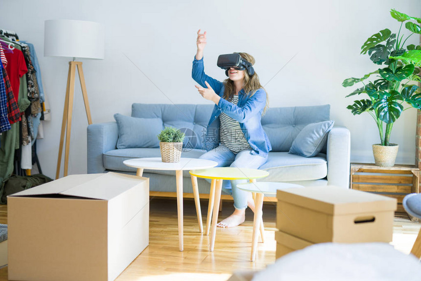 戴着虚拟现实眼镜的金发女郎坐在沙发上玩模拟游戏图片