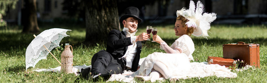 快乐的男人和女人坐在毯子上喝着葡萄酒图片