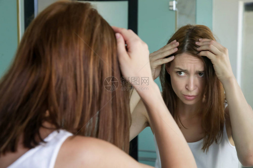 一位漂亮年轻女子在镜子前检查头皮和头发根颜色白发脱发或头皮干图片