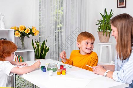 两个红头发的小男孩带着保姆母亲或老师坐在房间的桌子旁图片