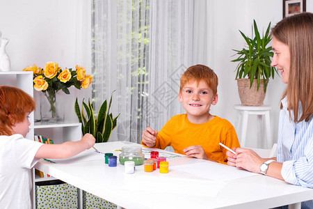 两个红头发的小男孩带着保姆母亲或老师坐在房间的桌子旁图片