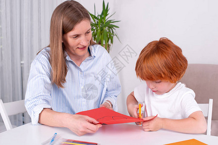 带着保姆母亲或老师的红发小男孩坐在房间的桌子旁图片