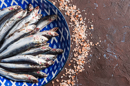 蓝鱼浅棕底深褐背景粉色盐的盘子中新鲜生凤尾鱼健康的蛋白质食品意背景图片