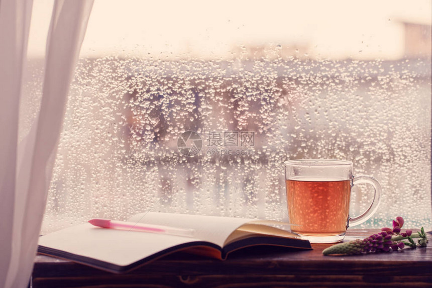 日落时有雨滴的窗户背景上的一杯茶图片
