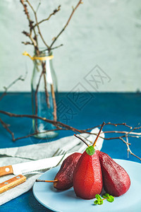 酒中的梨传统的甜点梨用红酒炖在蓝色混凝土表面的盘子上加巧克力酱浪漫晚餐甜点的概念简单的图片