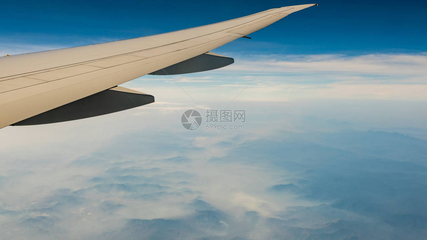 飞机的翼在有雾和薄雾的山盖上飞机在蓝天上飞行从飞机窗口的风景商业航空公司航班飞机翼飞行力图片