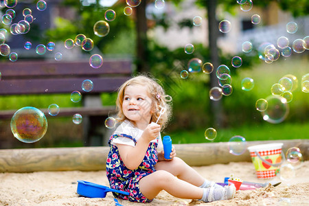 美丽的小金发蹒跚学步的女孩玩着吹肥皂泡鼓风机可爱的可爱宝贝孩子在阳光明媚的夏日在操场上玩耍快乐活跃有背景图片