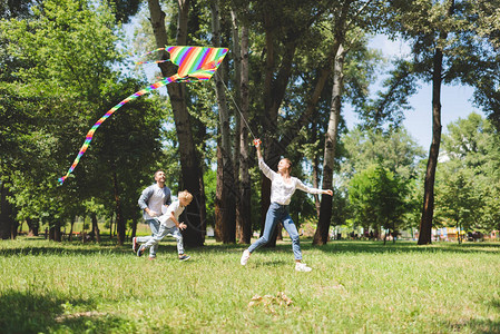 兴奋的家庭在公园里跑步和玩放风筝图片