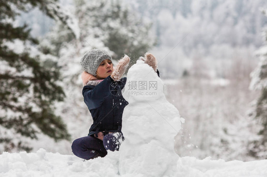 可爱的小女孩在冬天下雪的公园堆雪人图片
