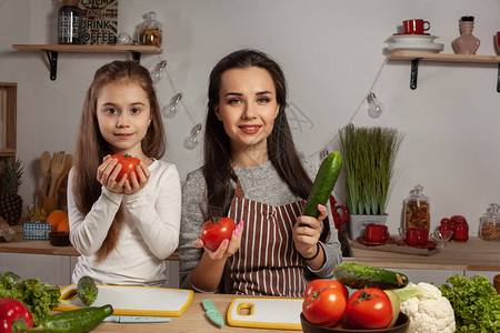 令人愉快的妈和她的小公主在厨房里摆着西红柿和黄瓜图片