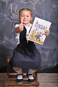 美丽微笑的年轻一年级学生坐在黑板背景上的书画像告别钟知识日学年开始学校设背景图片