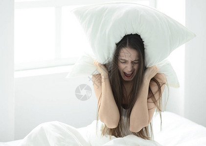 愤怒的年轻女子用枕头遮住耳朵图片