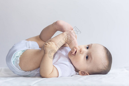 饥饿的小男孩把脚放在嘴里6个月大的婴儿在白色床上用品玩得开心可爱的宝躺在床上背景图片