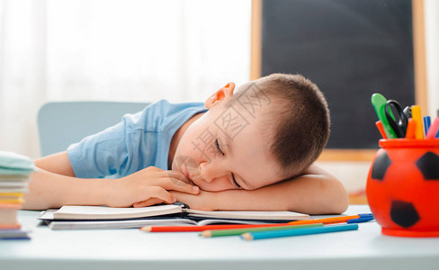 男生坐在家里的教室躺着桌子上摆满了书籍培训材料学童睡觉懒惰无聊缺乏能量疲劳概念沉迷和鬼背景图片