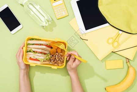 午餐盒上方装有塑料用具背包附近食物数字平板电脑瓶水和文具的妇女图片