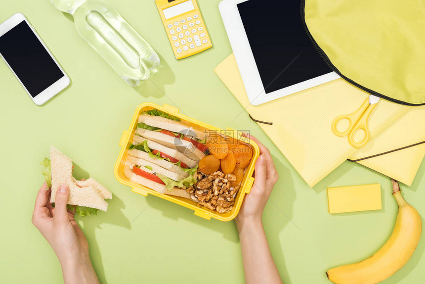 妇女手用三明治餐盒上装塑料用具背包附近食物数字平板电脑瓶水和图片