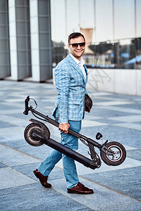 快乐的笑脸男人在去办公室时把新的电动摩托车折叠着图片