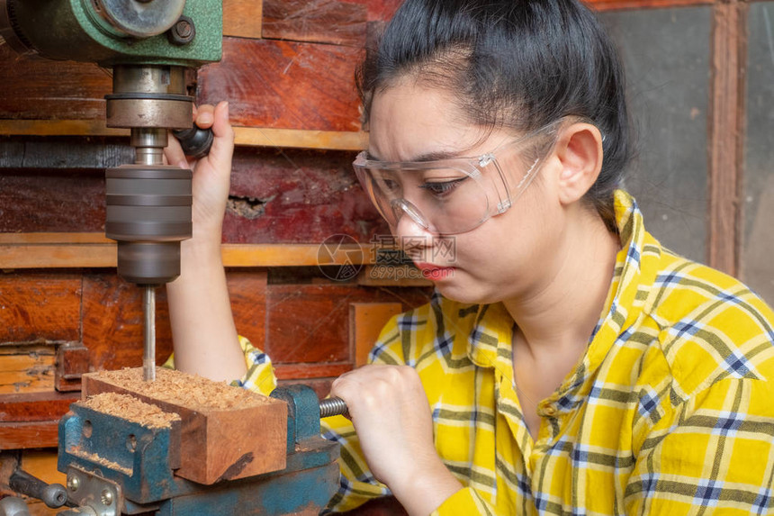 站立妇女正在工作台上与DrillPress在车间木匠机器上使用电动工具一起图片