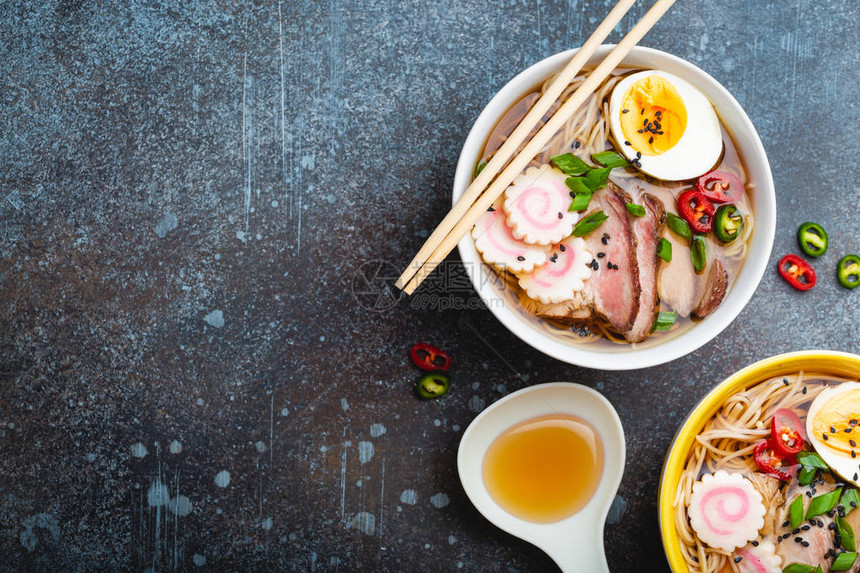 烹饪日本面条汤拉面拉面配猪肉片火影忍者鸡蛋厨房勺子和质朴的石头背景上的肉汤制作日本传统菜肴图片