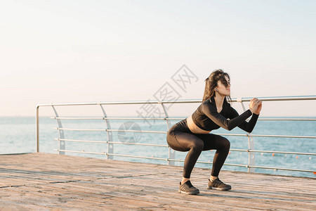 白无线耳机的棕色黑发年轻女子在日出时在码头进行锻炼图片