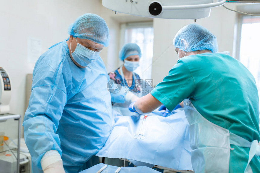 一位戴着面罩和长袍的经验丰富的外科医生在无菌手术室中与助理和麻图片