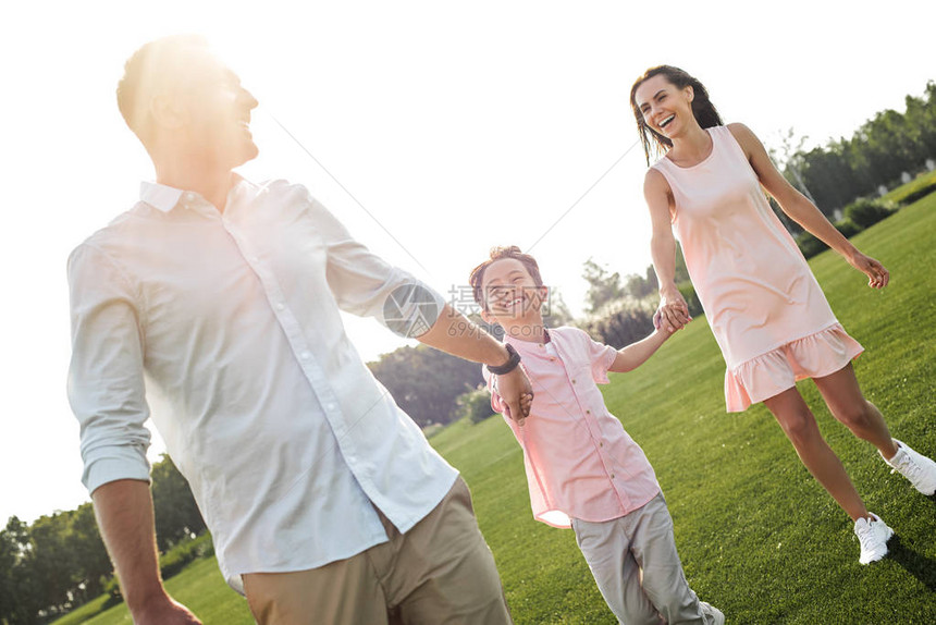 整个快乐的小男孩在公园里微笑和与父母一起走动图片
