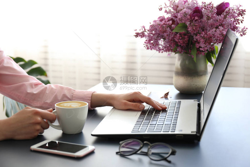 女人的手用黑色键盘在白色笔记本电脑上打字图片