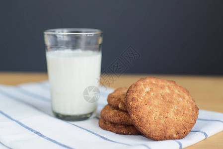 木桌上条纹白餐巾纸上圆形棕色全麦面粉饼干和牛奶玻璃的静物图片