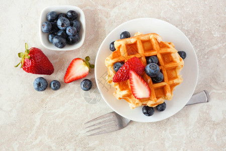 带草莓和蓝莓的早餐华夫饼在明亮石头背景图片